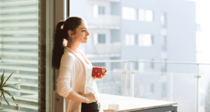 brunette woman standing in front of a window with coffee