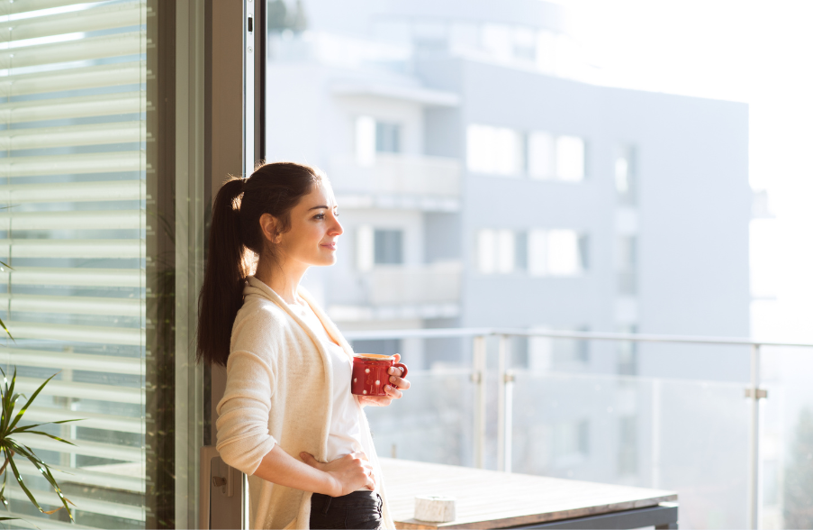 brunette woman standing in front of a window with coffee