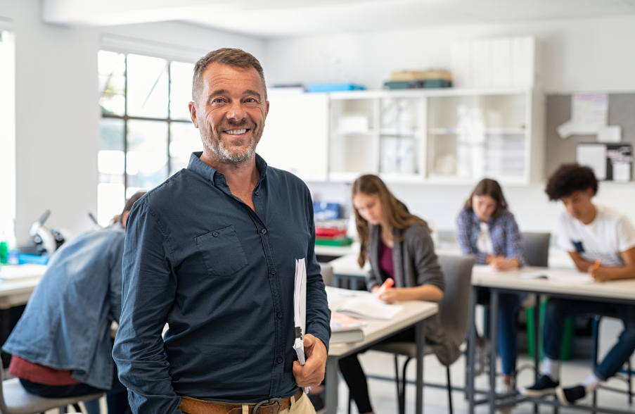 teacher smiling at front of classroom holding books