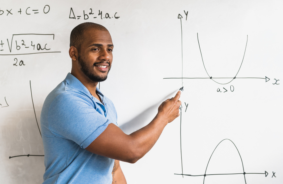 man in blue shirt standing at front of class teaching math