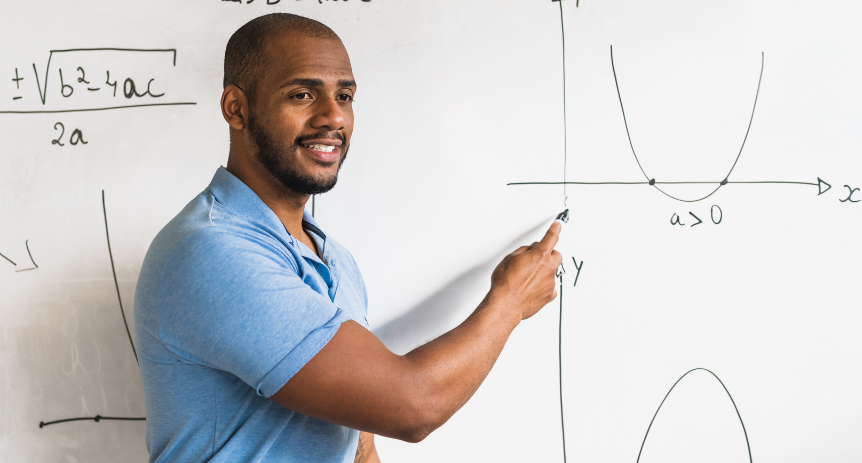 man in blue shirt standing at front of class teaching math