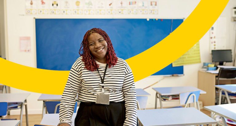 Female substitute teacher sitting at desk smiling.