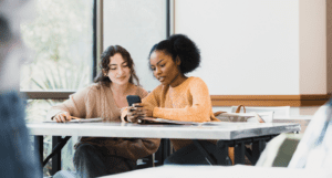 two young people sitting in a classroom on their phones