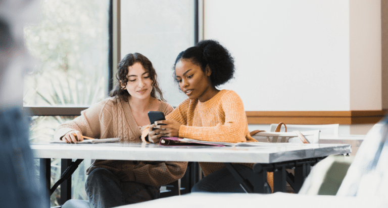 two young people sitting in a classroom on their phones