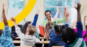 smiling teacher in front of class raising hands