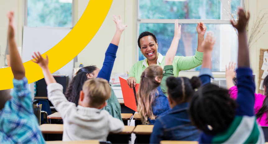 smiling teacher in front of class raising hands